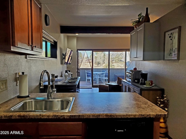 kitchen with a textured ceiling, a textured wall, a peninsula, a sink, and brown cabinets