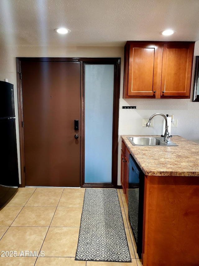 kitchen with light tile patterned floors, light countertops, brown cabinetry, a sink, and black appliances