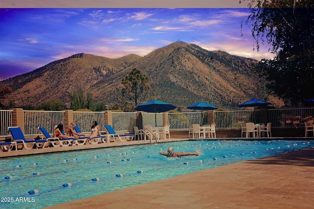 pool at dusk with a patio, a mountain view, and a community pool