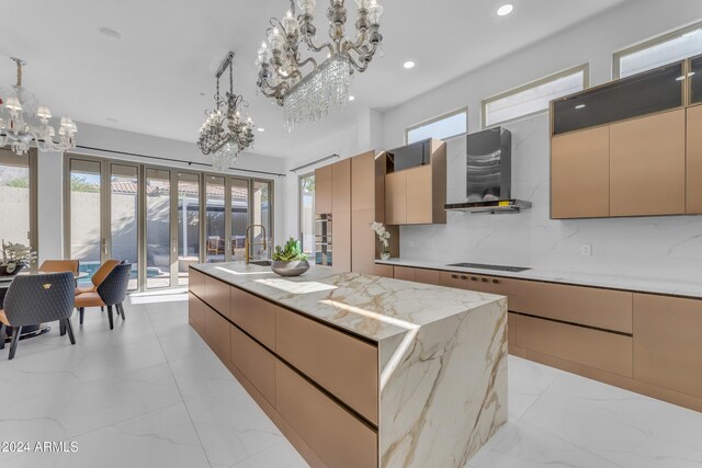 kitchen with a large island with sink, tasteful backsplash, a chandelier, and wall chimney range hood