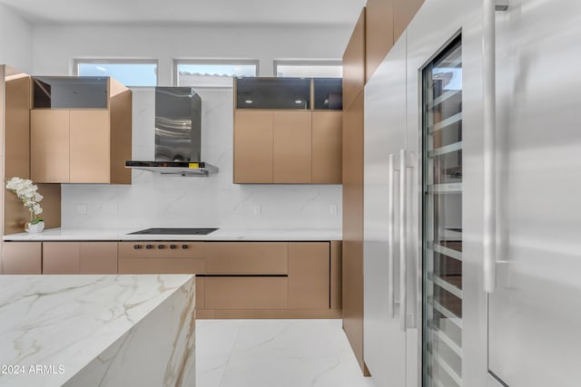 kitchen with black electric cooktop, light stone counters, wall chimney exhaust hood, tasteful backsplash, and stainless steel refrigerator