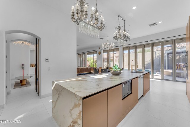 kitchen featuring light stone countertops, a center island with sink, decorative light fixtures, and stainless steel microwave