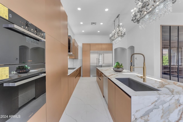 kitchen featuring light stone counters, a center island with sink, appliances with stainless steel finishes, hanging light fixtures, and sink