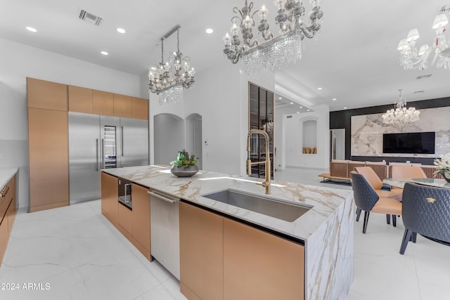 kitchen featuring light stone counters, sink, appliances with stainless steel finishes, a large island with sink, and decorative light fixtures