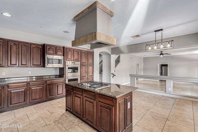 kitchen with hanging light fixtures, ceiling fan, dark stone counters, stainless steel appliances, and a center island