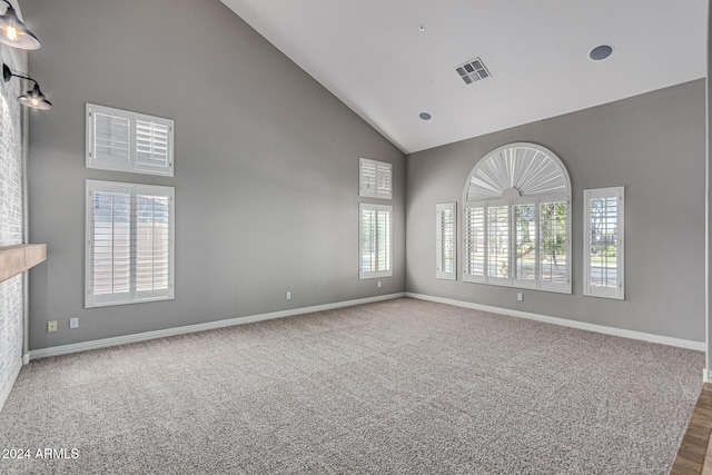 carpeted spare room with high vaulted ceiling