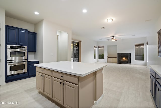 3551 W Hidden Mountain Ln, Anthem, AZ 85086 - kitchen featuring a kitchen island, a fireplace, stainless steel double oven, light countertops, and a ceiling fan
