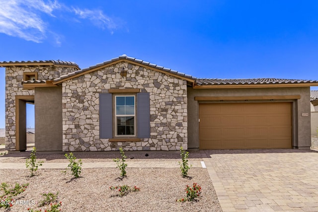 view of front of property featuring a tiled roof, decorative driveway, a garage, and stucco siding