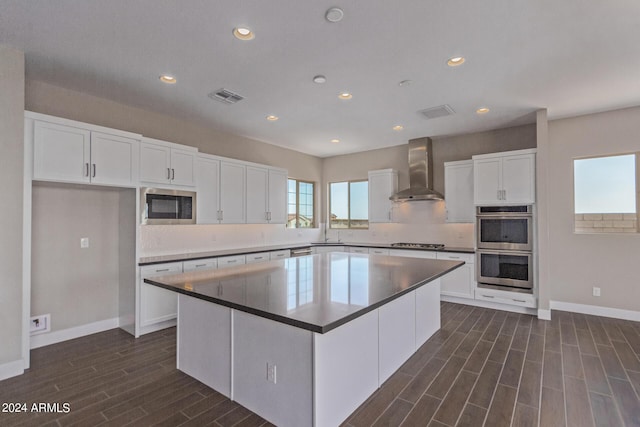 kitchen with stainless steel appliances, a kitchen island, dark wood-type flooring, wall chimney range hood, and white cabinetry