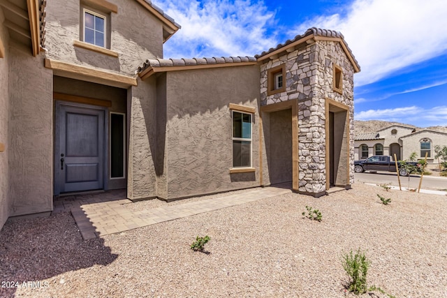 exterior space featuring a tiled roof, stone siding, and stucco siding