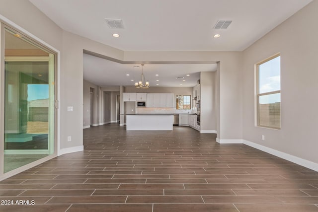 unfurnished living room with a healthy amount of sunlight, dark hardwood / wood-style floors, and an inviting chandelier