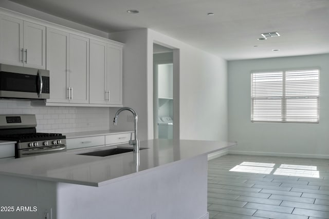 kitchen featuring sink, washer and clothes dryer, stainless steel appliances, tasteful backsplash, and white cabinets