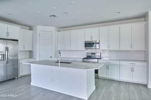 kitchen with an island with sink, sink, white cabinets, backsplash, and stainless steel appliances