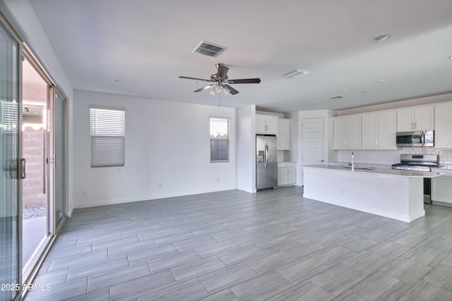 kitchen with white cabinetry, a center island with sink, ceiling fan, stainless steel appliances, and backsplash