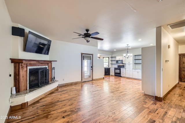 unfurnished living room featuring ceiling fan with notable chandelier, a fireplace, and light hardwood / wood-style flooring