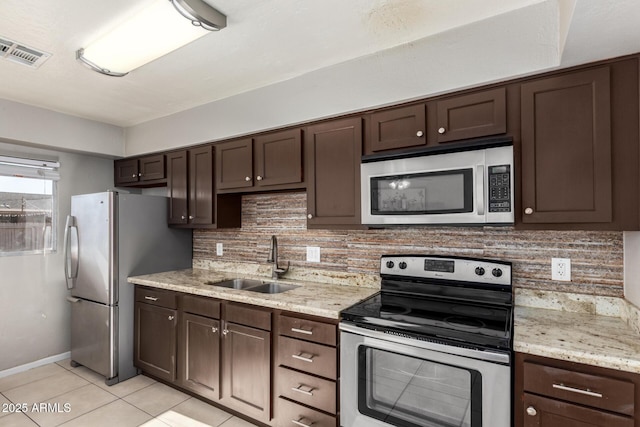 kitchen featuring sink, stainless steel appliances, light tile patterned floors, dark brown cabinets, and light stone counters