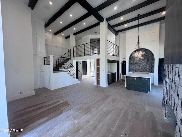 unfurnished living room with light wood-style floors, beamed ceiling, a towering ceiling, recessed lighting, and stairs