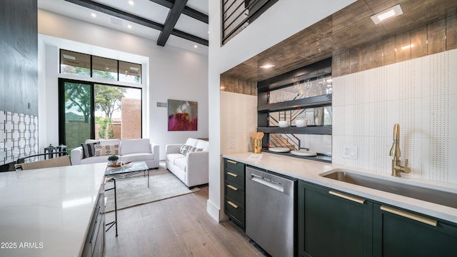 kitchen featuring light countertops, beam ceiling, stainless steel dishwasher, a sink, and wood finished floors