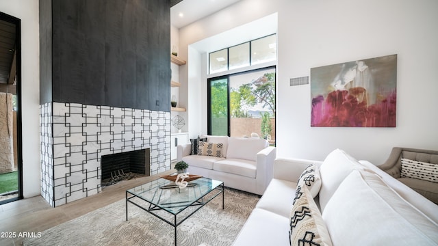 living room with visible vents, light wood-type flooring, a fireplace, recessed lighting, and a towering ceiling
