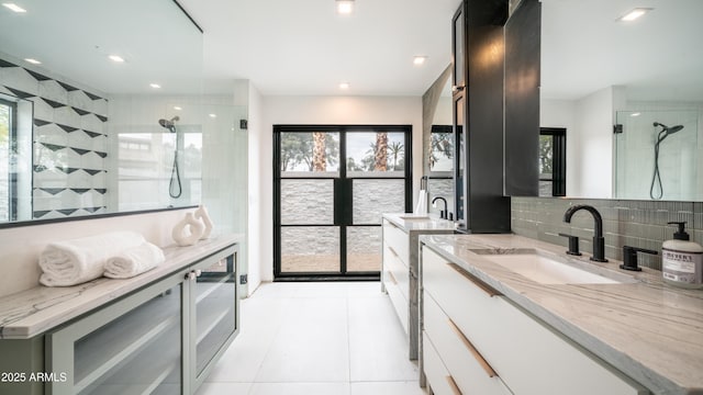 full bath with two vanities, a sink, a wealth of natural light, decorative backsplash, and a tile shower