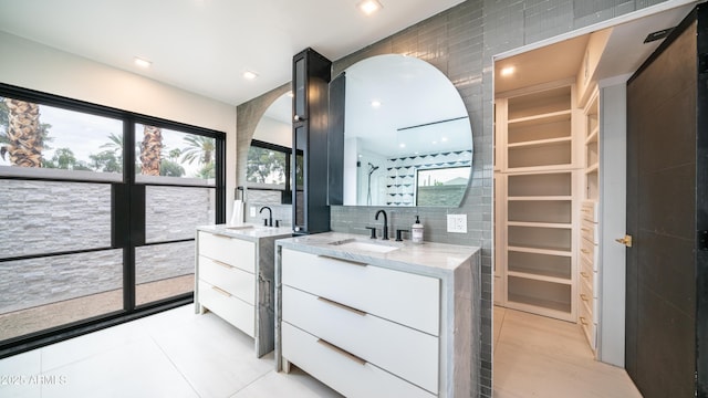 bathroom featuring two vanities, a sink, a spacious closet, and tile walls