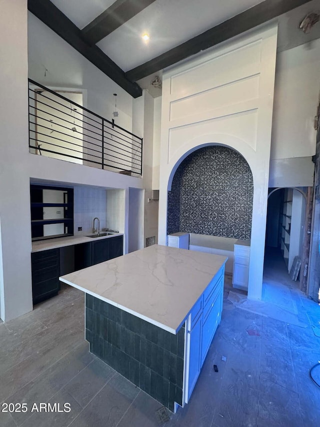 kitchen with a sink, a towering ceiling, and light stone countertops