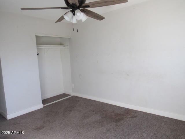 unfurnished bedroom featuring ceiling fan, a closet, and dark colored carpet