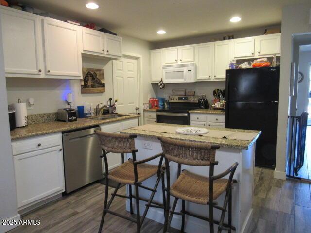 kitchen with white cabinetry, stainless steel appliances, a kitchen breakfast bar, dark wood-type flooring, and light stone counters