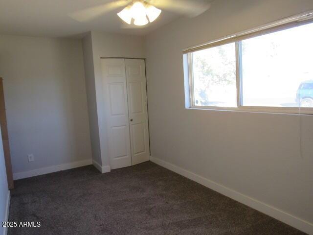 unfurnished bedroom featuring ceiling fan, dark carpet, and a closet