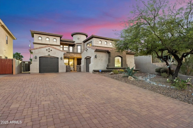 mediterranean / spanish-style house featuring an attached garage, a gate, fence, decorative driveway, and stucco siding