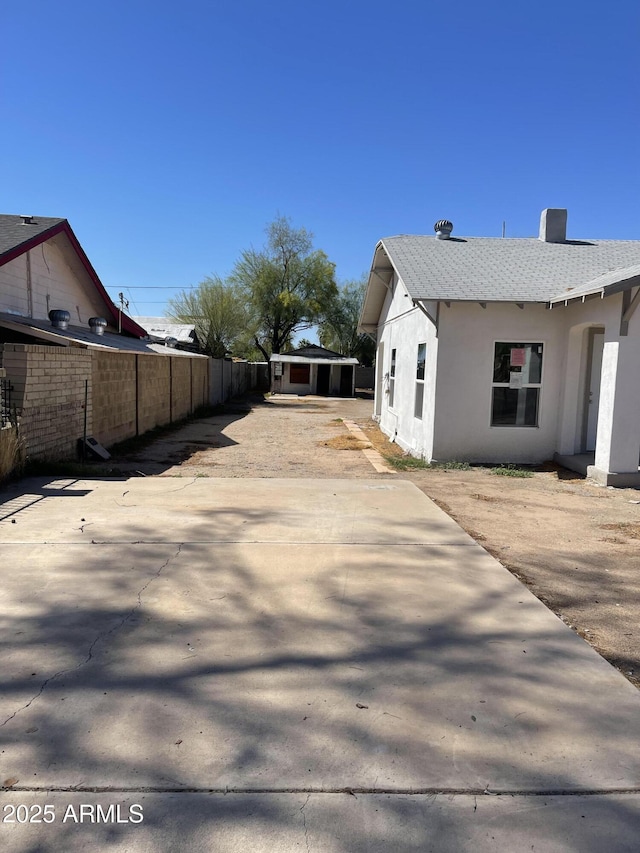 view of property exterior with a shingled roof, stucco siding, and fence