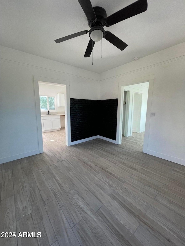 spare room featuring wood finished floors, ceiling fan, baseboards, and a sink