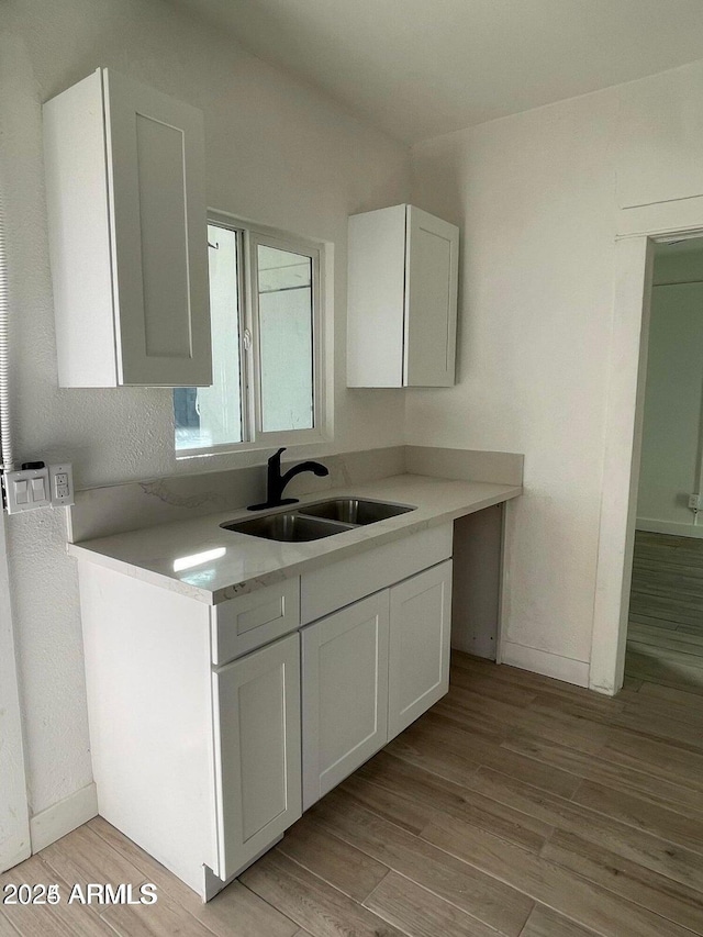 kitchen with baseboards, light wood-style floors, light countertops, and a sink