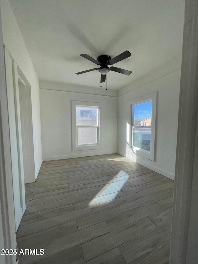 empty room featuring wood finished floors, a ceiling fan, and baseboards