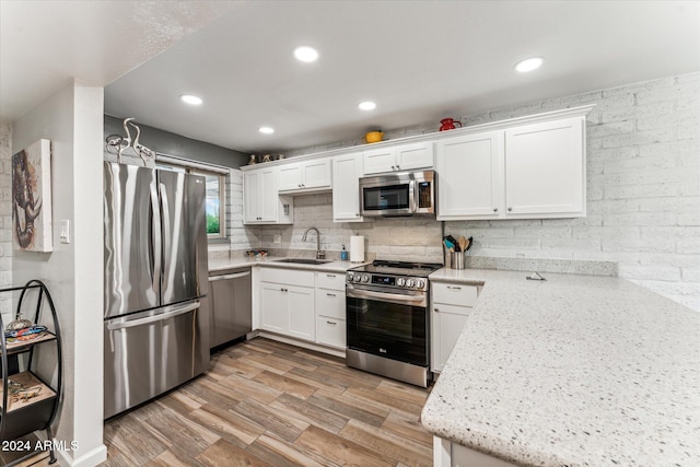 kitchen with sink, appliances with stainless steel finishes, white cabinetry, and light hardwood / wood-style floors