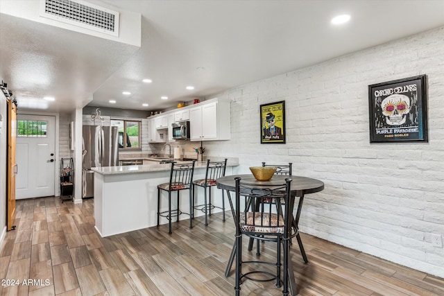 kitchen featuring light wood-type flooring, a barn door, kitchen peninsula, stainless steel appliances, and white cabinets