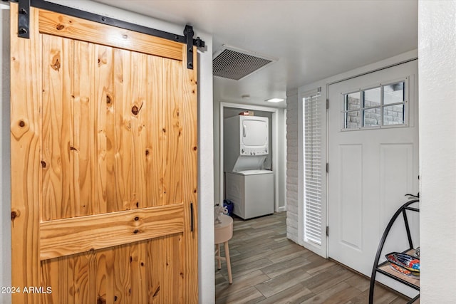 hallway featuring stacked washer / dryer, wood-type flooring, and a barn door