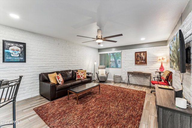 living room featuring light hardwood / wood-style flooring, brick wall, and ceiling fan