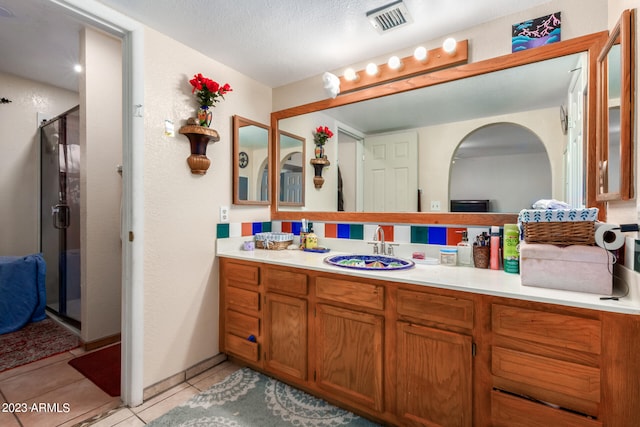 bathroom with a textured ceiling, tile flooring, a shower with shower door, and vanity