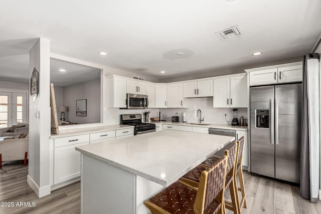 7440 E Hubbell St, Scottsdale, AZ 85257 - kitchen with appliances with stainless steel finishes, light wood-type flooring, a breakfast bar, white cabinetry, and recessed lighting