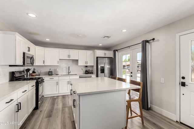7440 E Hubbell St, Scottsdale, AZ 85257 - kitchen featuring stainless steel appliances, decorative backsplash, a breakfast bar area, light wood finished floors, and white cabinetry