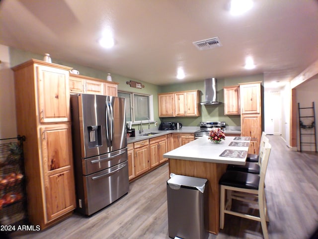 kitchen featuring light wood-type flooring, wall chimney exhaust hood, a breakfast bar, stainless steel appliances, and a kitchen island