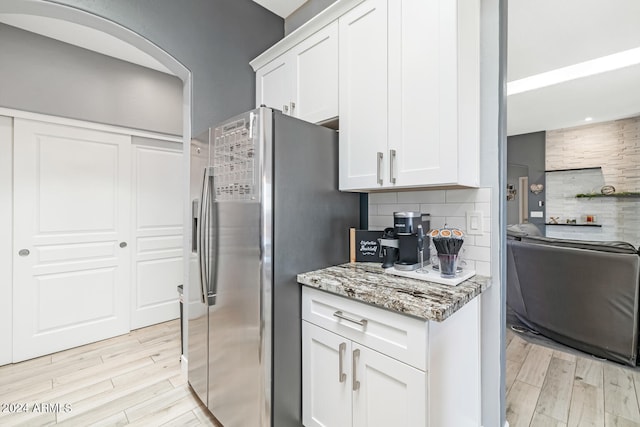 kitchen with white cabinets, stainless steel refrigerator with ice dispenser, decorative backsplash, light hardwood / wood-style flooring, and light stone countertops