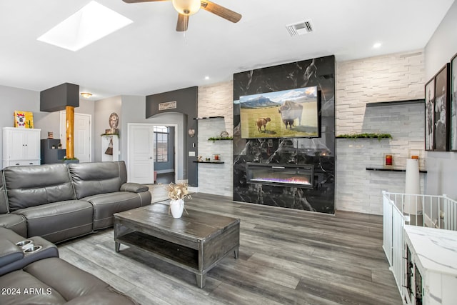 living room with a large fireplace, ceiling fan, a skylight, and hardwood / wood-style floors