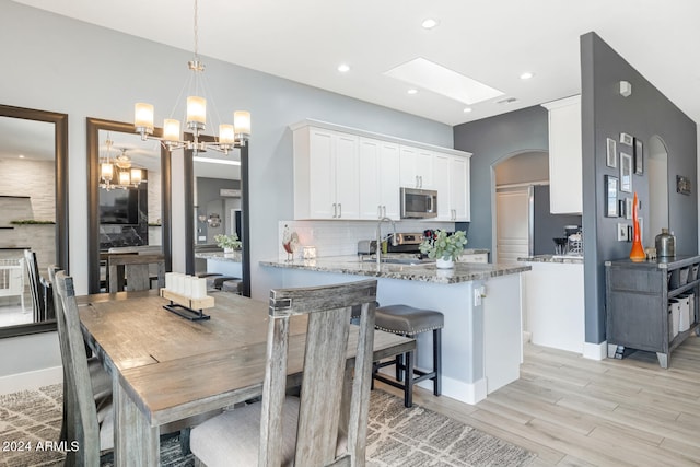 dining space with a skylight, sink, light hardwood / wood-style floors, and a chandelier