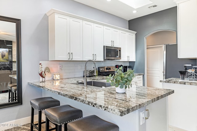 kitchen with white cabinets, sink, backsplash, appliances with stainless steel finishes, and light stone countertops