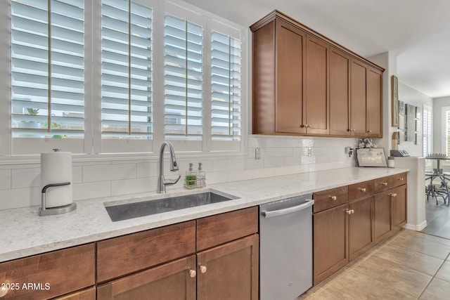 kitchen with light tile patterned flooring, sink, decorative backsplash, stainless steel dishwasher, and light stone counters