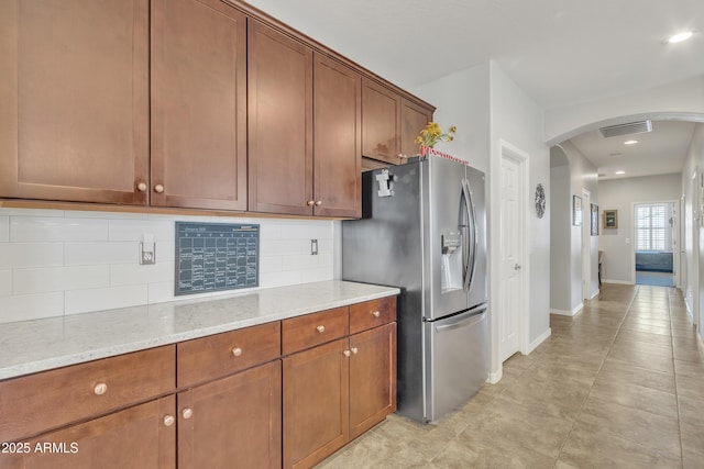 kitchen with stainless steel refrigerator with ice dispenser, backsplash, and light stone counters