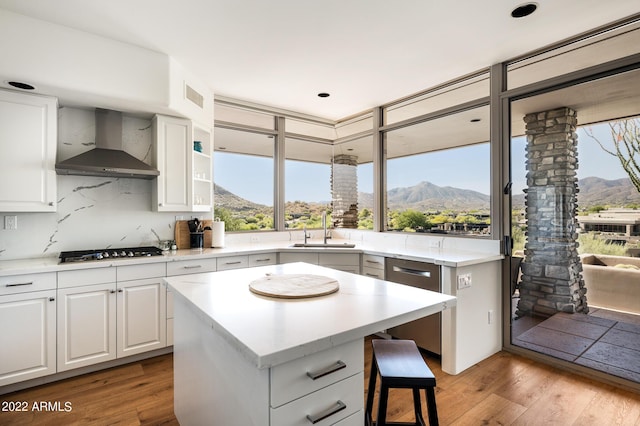 kitchen with a kitchen island, sink, white cabinets, a mountain view, and wall chimney range hood