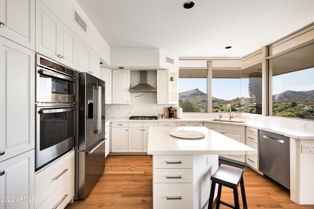 kitchen with a kitchen island, sink, stainless steel appliances, a mountain view, and wall chimney range hood